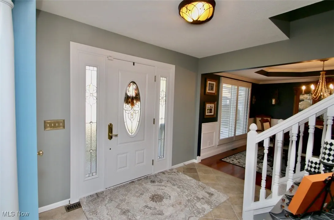 Entryway featuring light tile patterned floors, wainscoting, and a chandelier