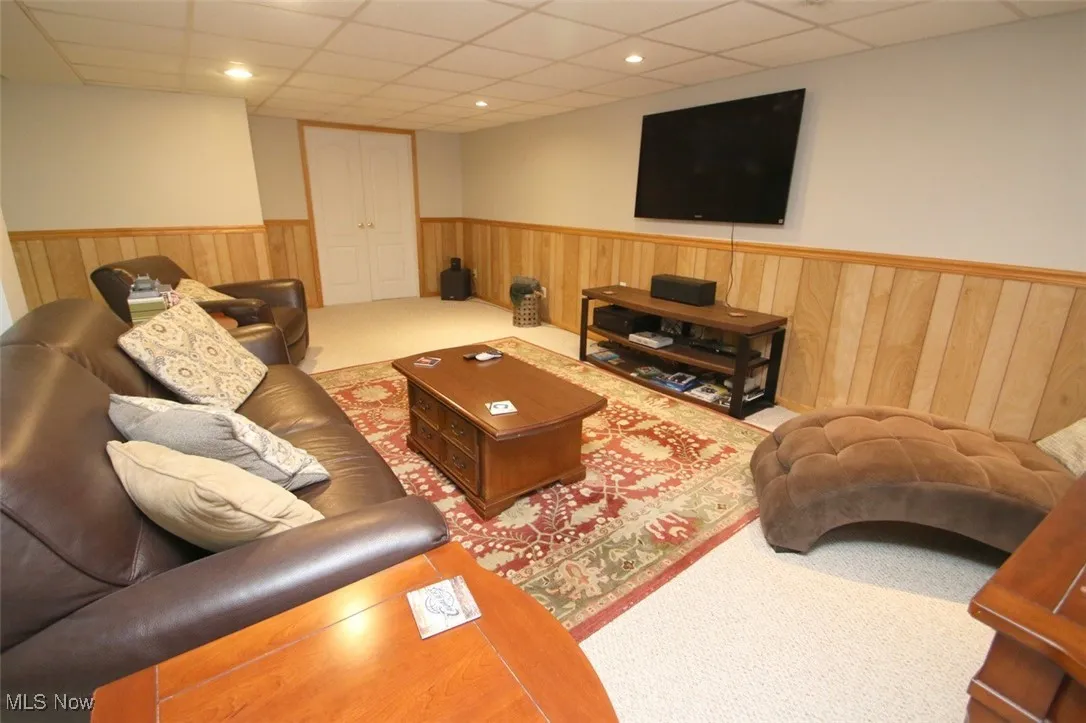 Living room with a drop ceiling, wood walls, carpet floors, a wainscoted wall, and recessed lighting