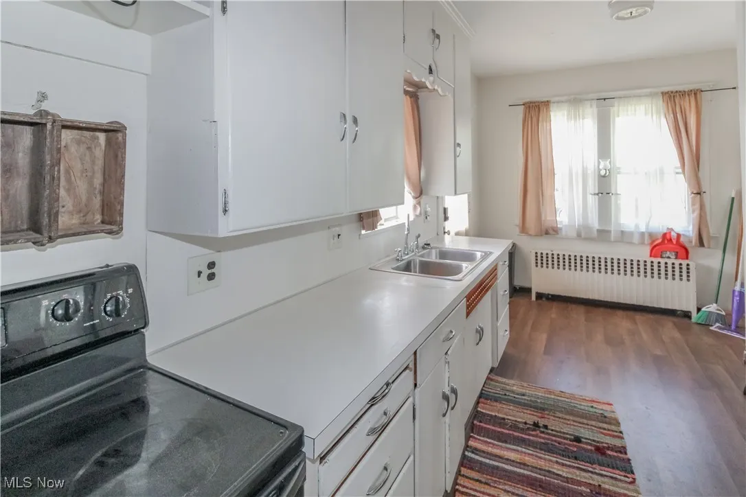 Kitchen with black electric range, white cabinetry, light countertops, dark wood-type flooring, and radiator