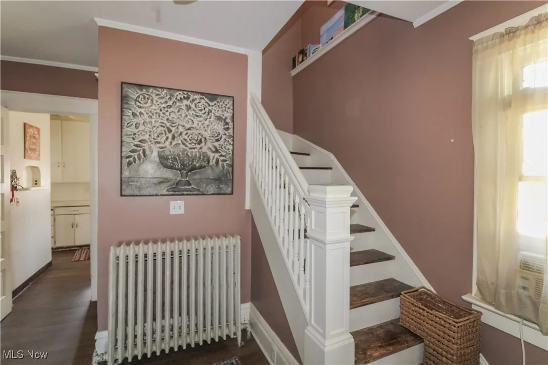 Stairway with radiator, crown molding, and wood finished floors