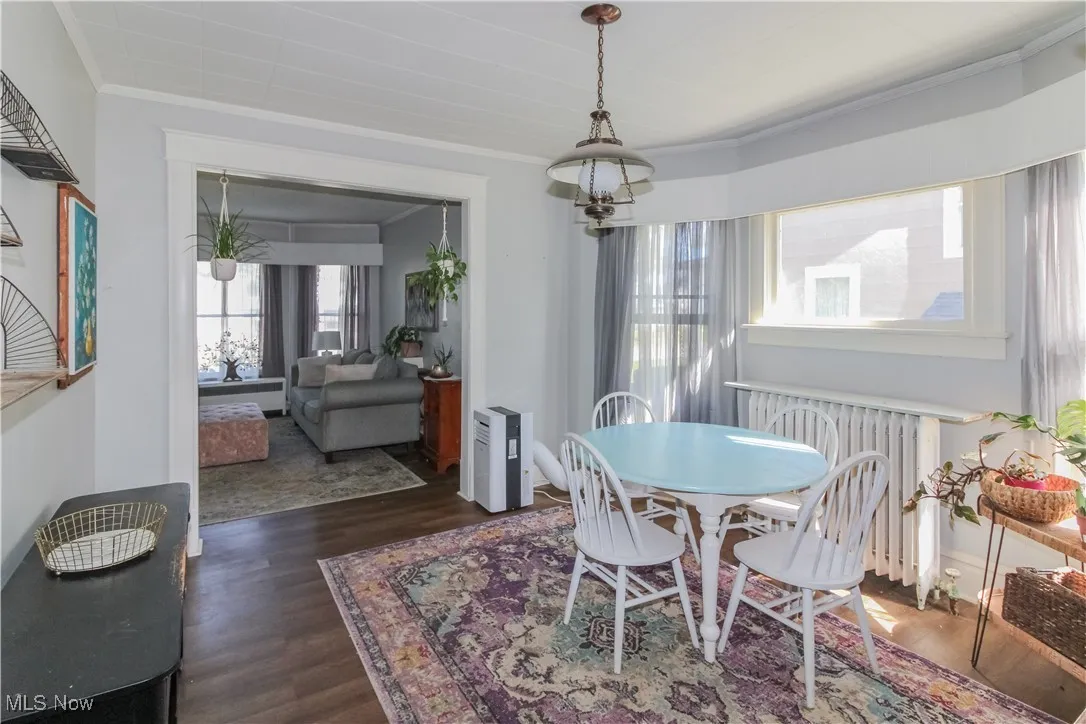 Dining space with radiator heating unit, crown molding, and dark wood finished floors