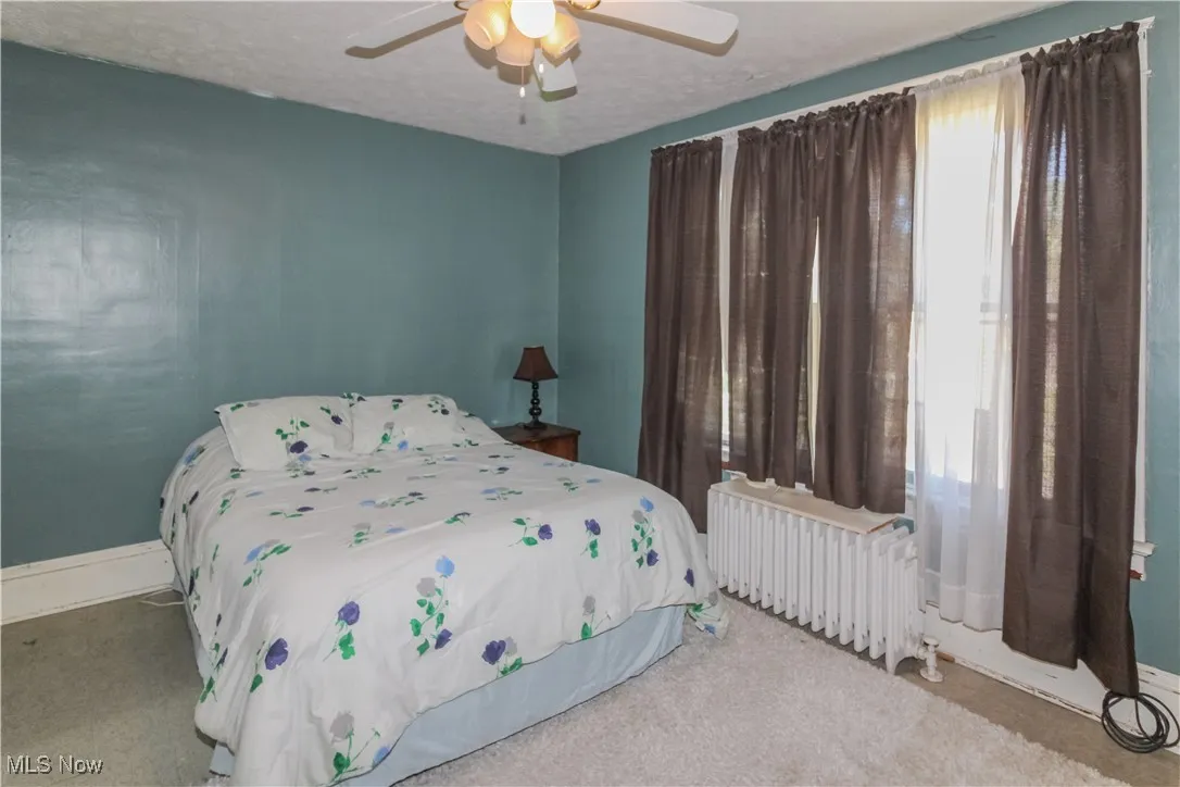 Carpeted bedroom featuring radiator, a ceiling fan, and a textured ceiling