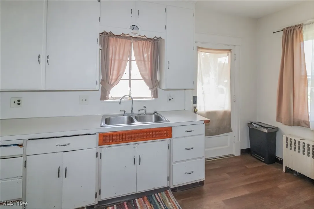 Kitchen featuring light countertops, white cabinets, dark wood-type flooring, and radiator heating unit