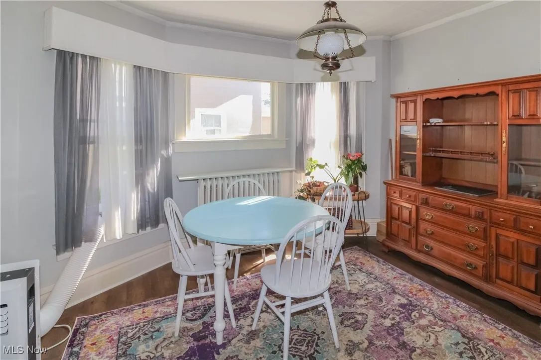Dining room featuring dark wood-style floors, crown molding, and radiator heating unit