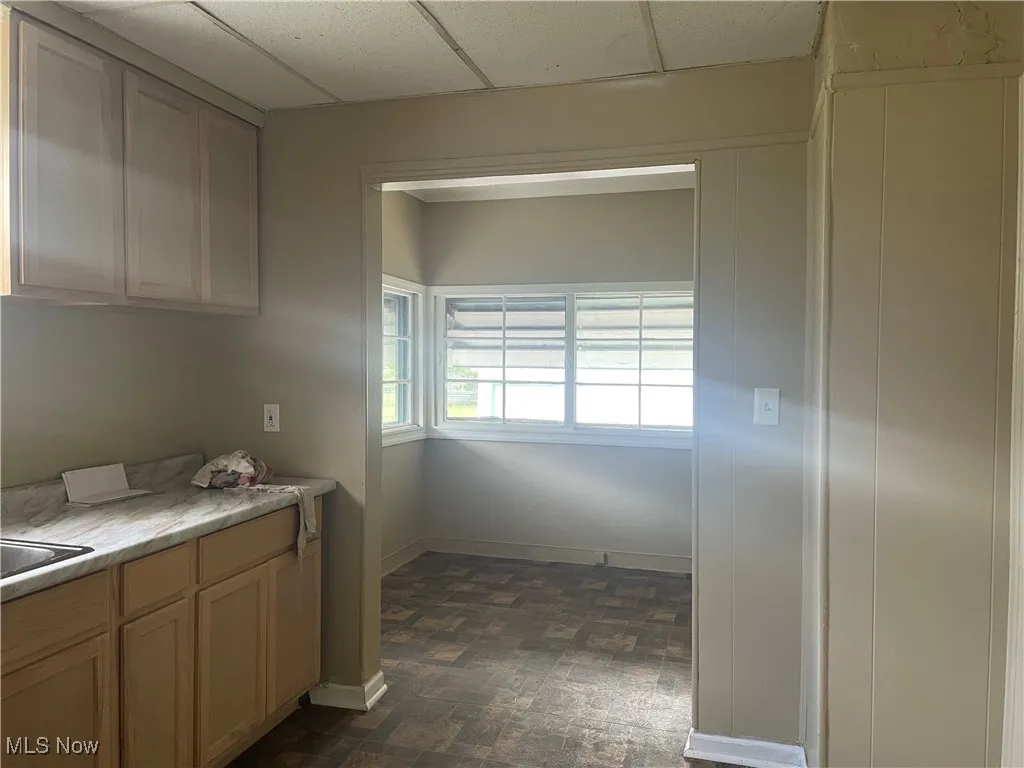 Kitchen with light countertops, a paneled ceiling, stone finish floors, and light brown cabinetry