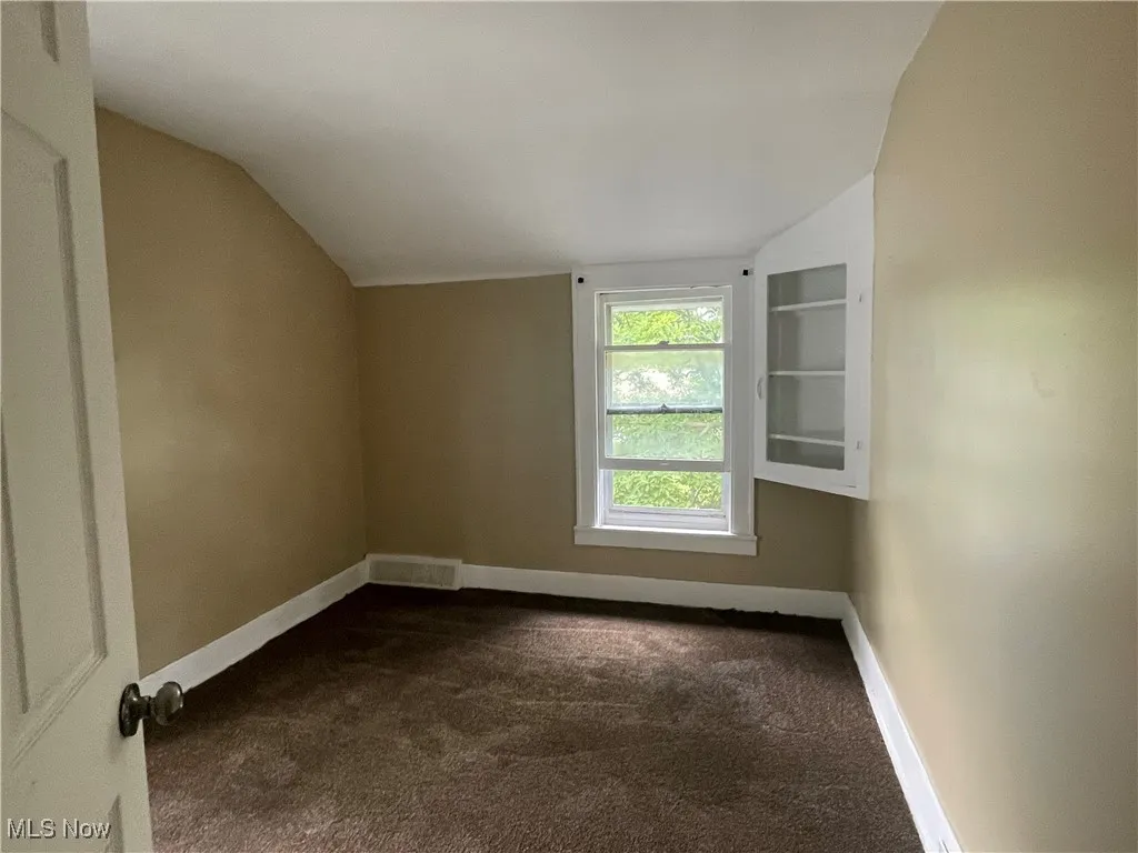 Bonus room with dark colored carpet and vaulted ceiling