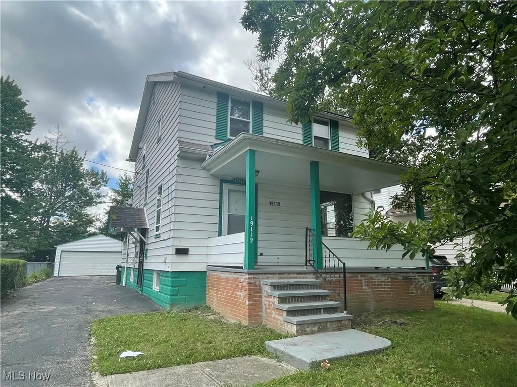 View of front of home featuring covered porch, an outbuilding, a front yard, and a garage