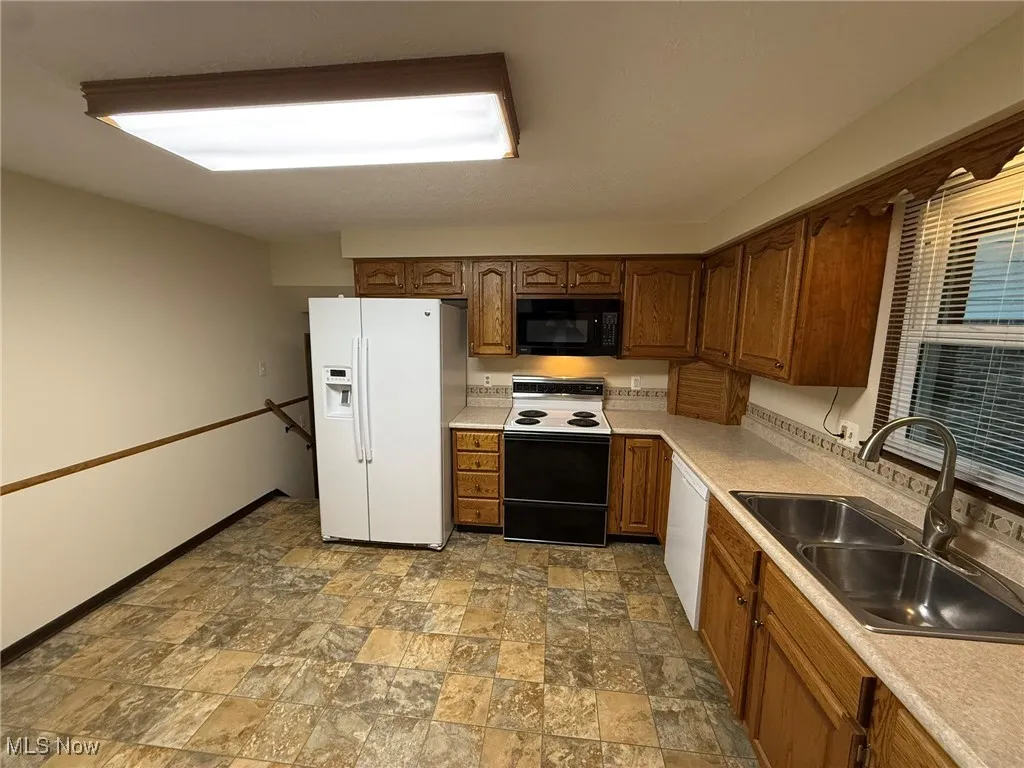 Kitchen featuring white appliances, stone finish flooring, light countertops, and brown cabinetry