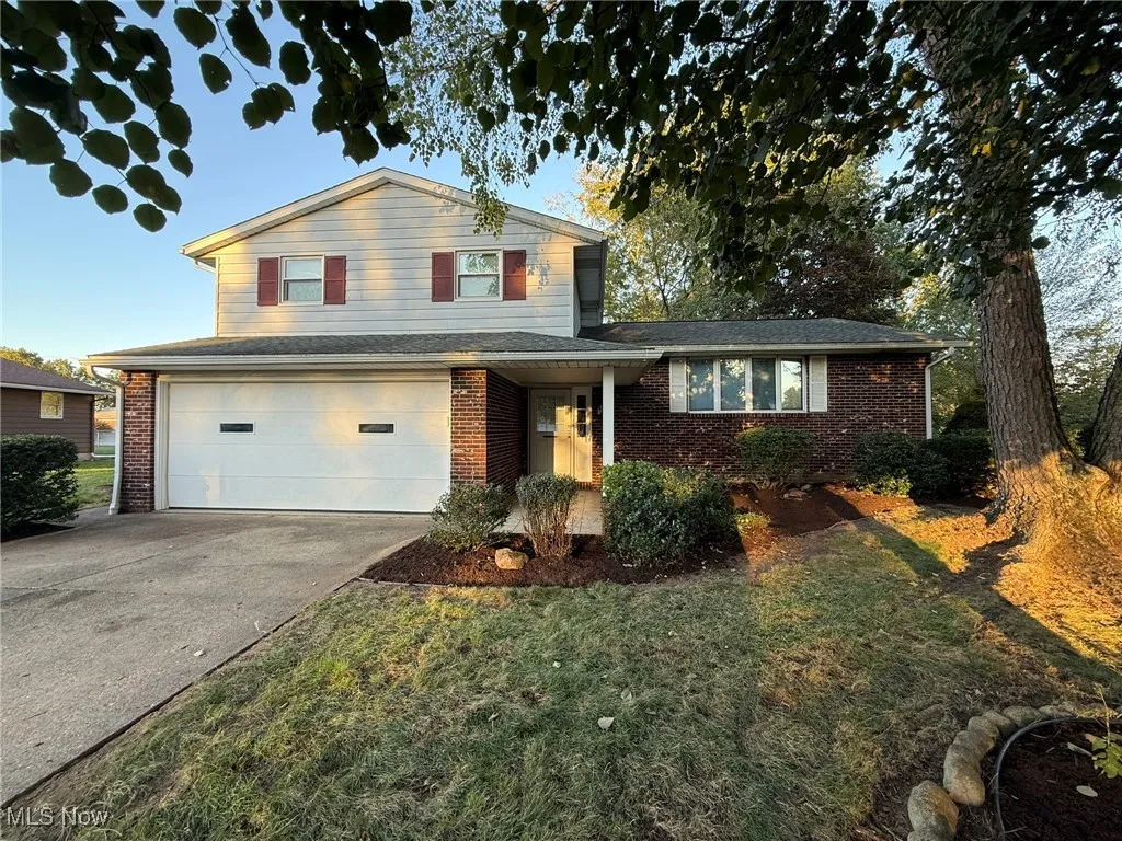 Split level home featuring a garage, concrete driveway, a front lawn, and brick siding