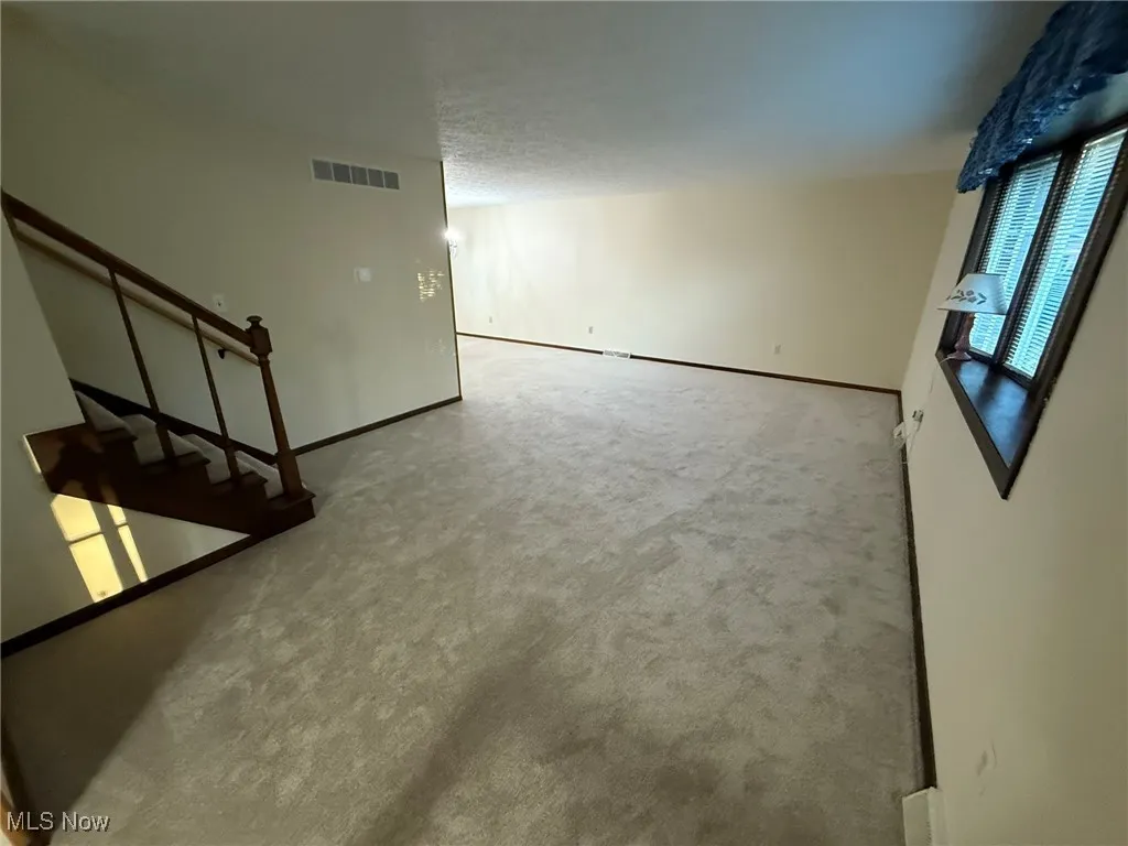 Unfurnished living room with light colored carpet and stairway