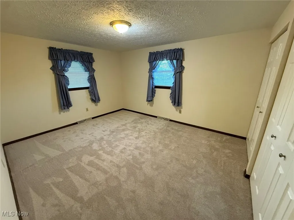 Unfurnished bedroom featuring multiple windows, carpet, and a textured ceiling
