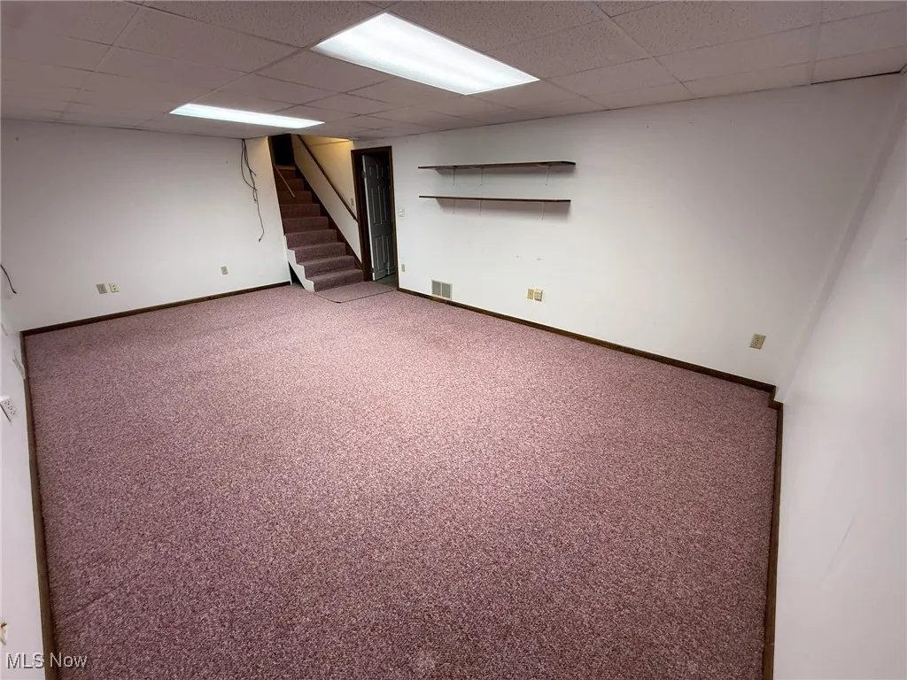 Finished below grade area with stairs, carpet floors, and a drop ceiling