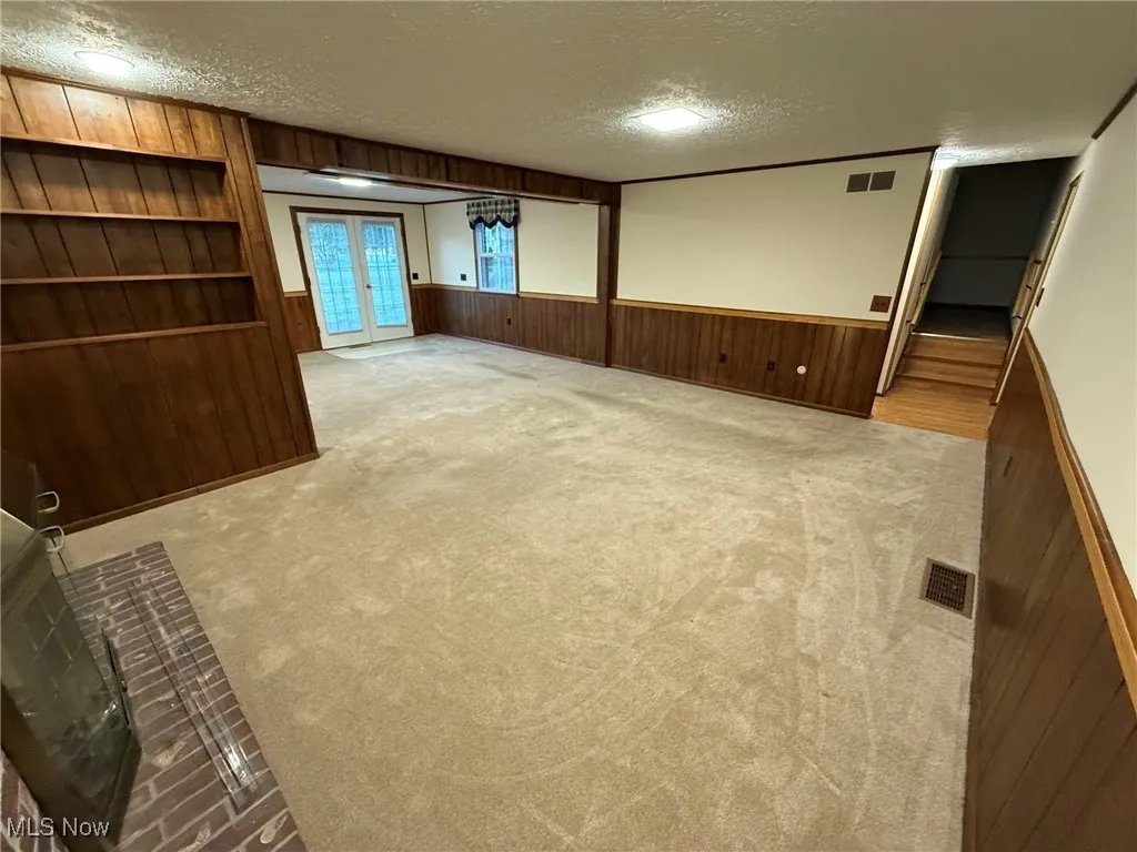 Unfurnished room with a textured ceiling, wooden walls, light colored carpet, and french doors