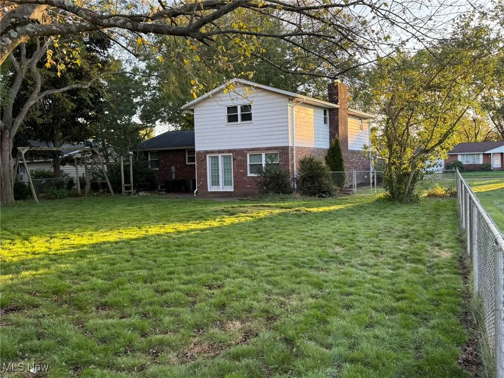 View of side of home featuring brick siding, a chimney, french doors, and a fenced backyard