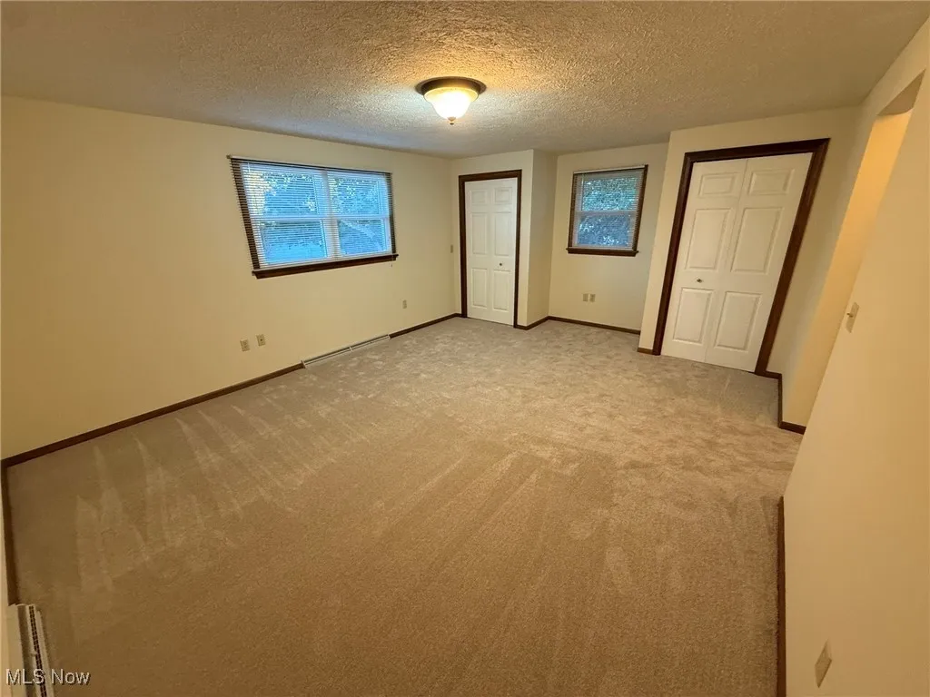 Unfurnished bedroom featuring multiple closets, carpet, a textured ceiling, and a baseboard radiator