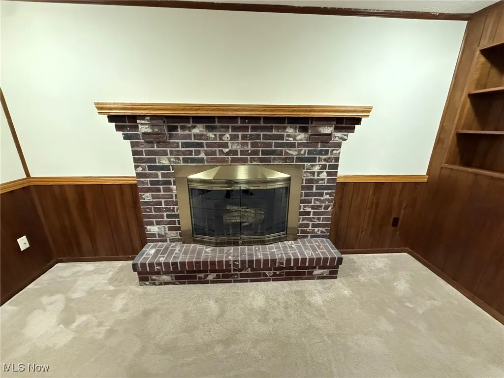 Detailed view of wood walls, wainscoting, a brick fireplace, carpet flooring, and built in features