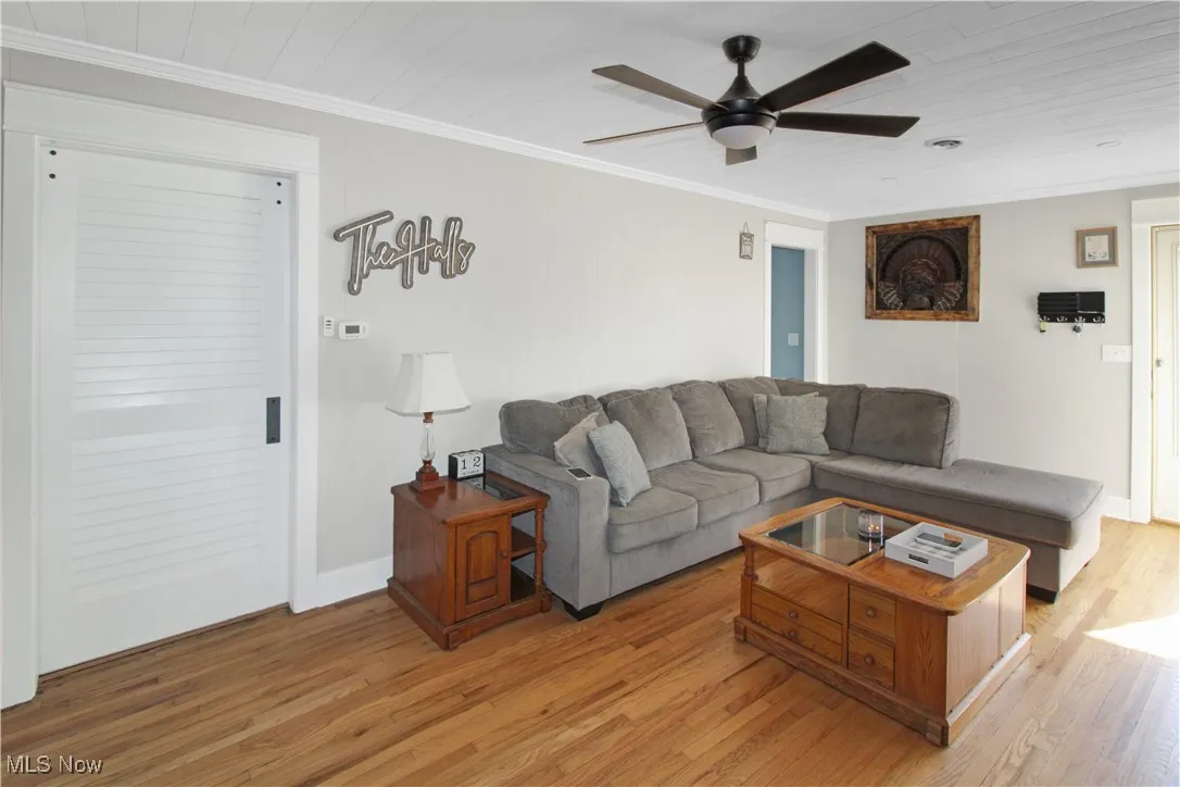 Living area with light wood-style floors, ornamental molding, and a ceiling fan