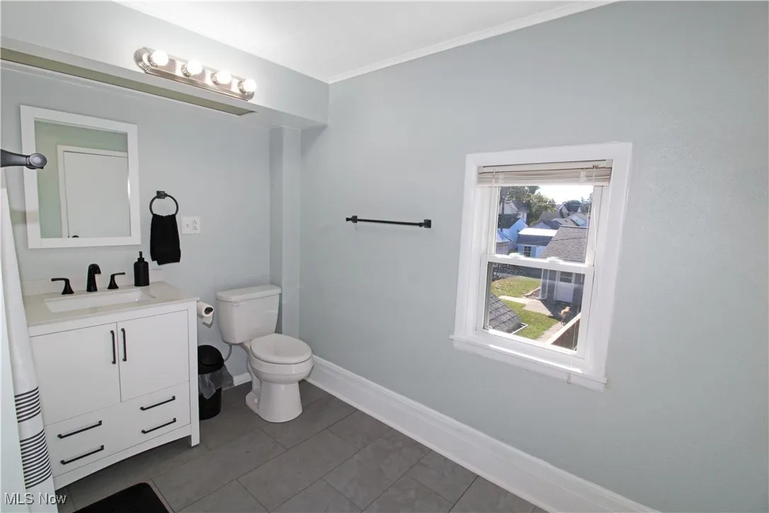 Half bath featuring vanity, ornamental molding, and light tile patterned flooring