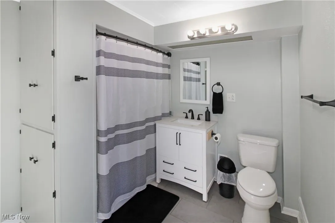 Full bathroom with light tile patterned flooring, a shower with shower curtain, vanity, and crown molding