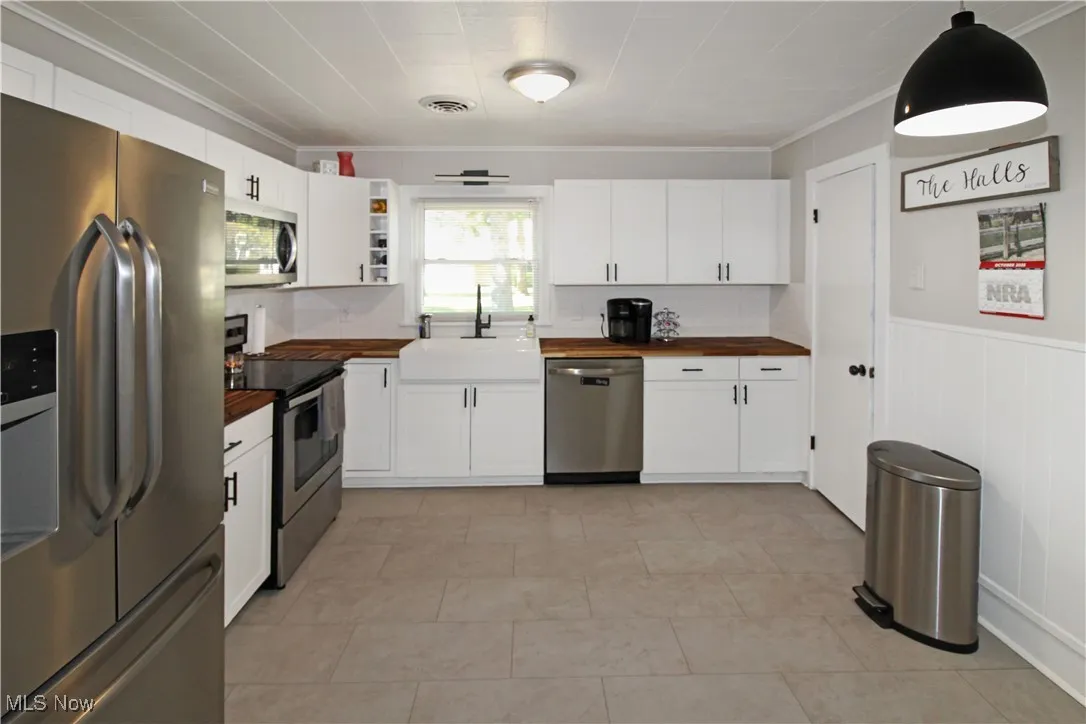 Kitchen featuring stainless steel appliances, wooden counters, ornamental molding, decorative backsplash, and white cabinets