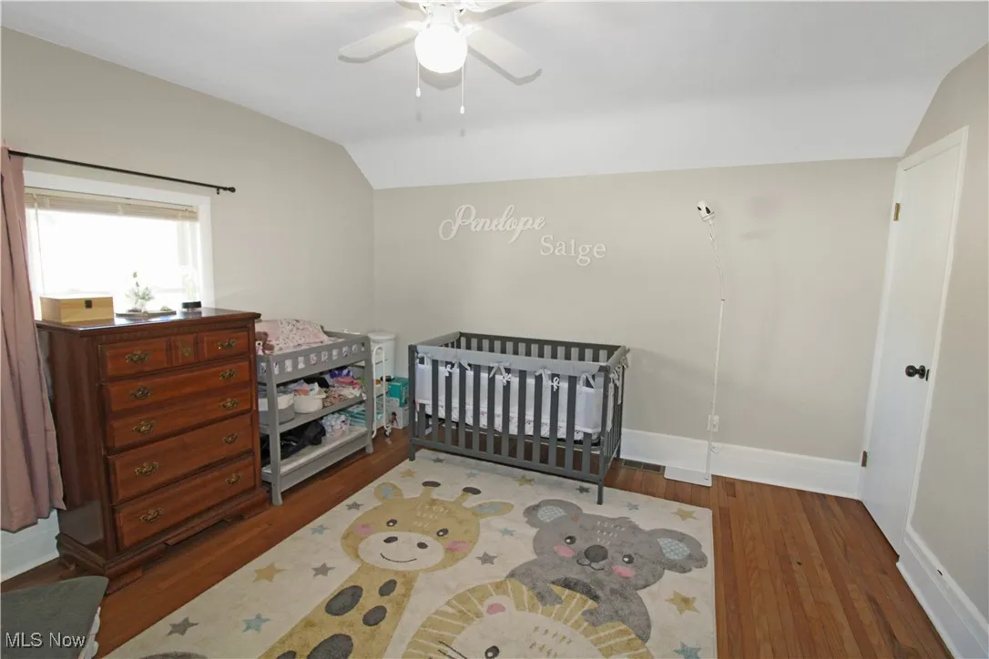 Bedroom featuring hardwood / wood-style flooring, a crib, vaulted ceiling, and ceiling fan