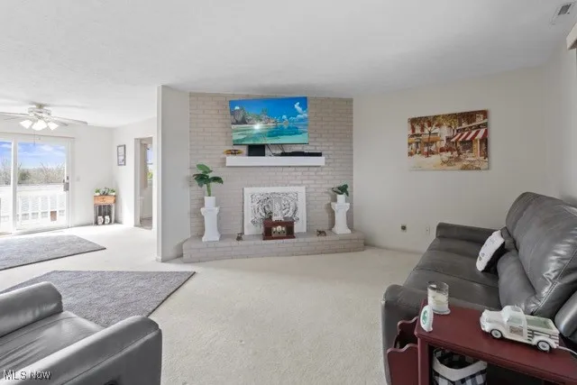 Living room with carpet flooring, ceiling fan, a fireplace, and a textured ceiling
