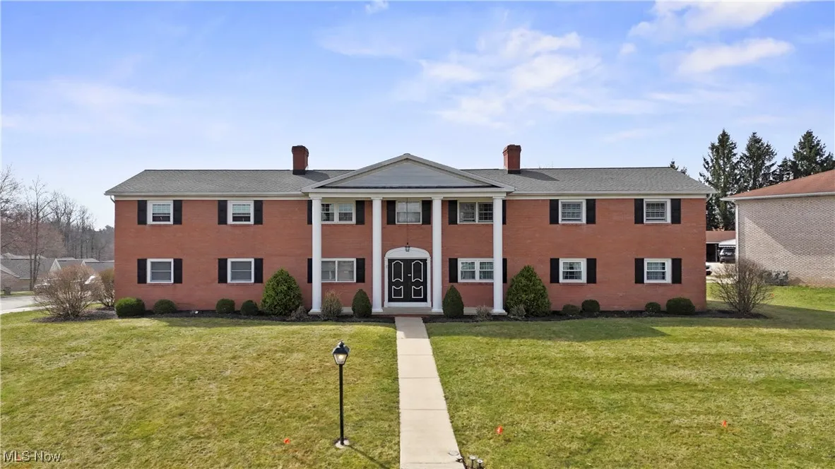Neoclassical / greek revival condominium featuring a chimney, a front lawn, and brick siding