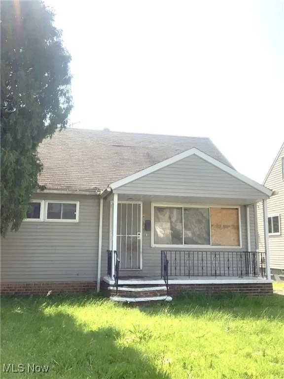 View of front of home with covered porch, a front yard, and a shingled roof