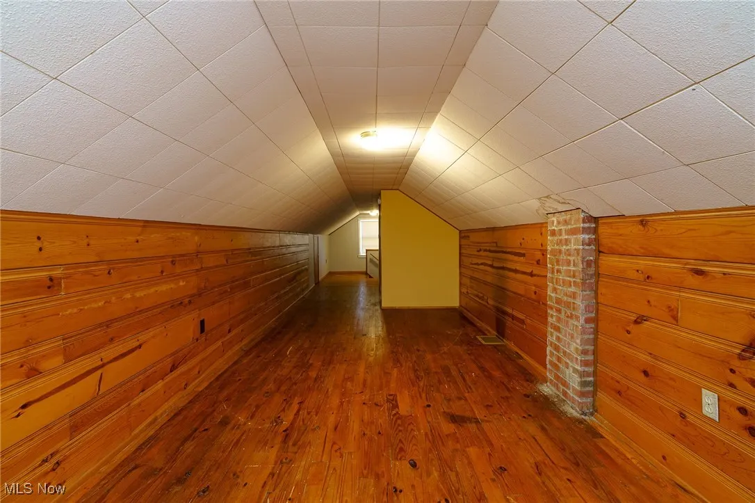 Bonus room with dark wood-style floors, wooden walls, and lofted ceiling