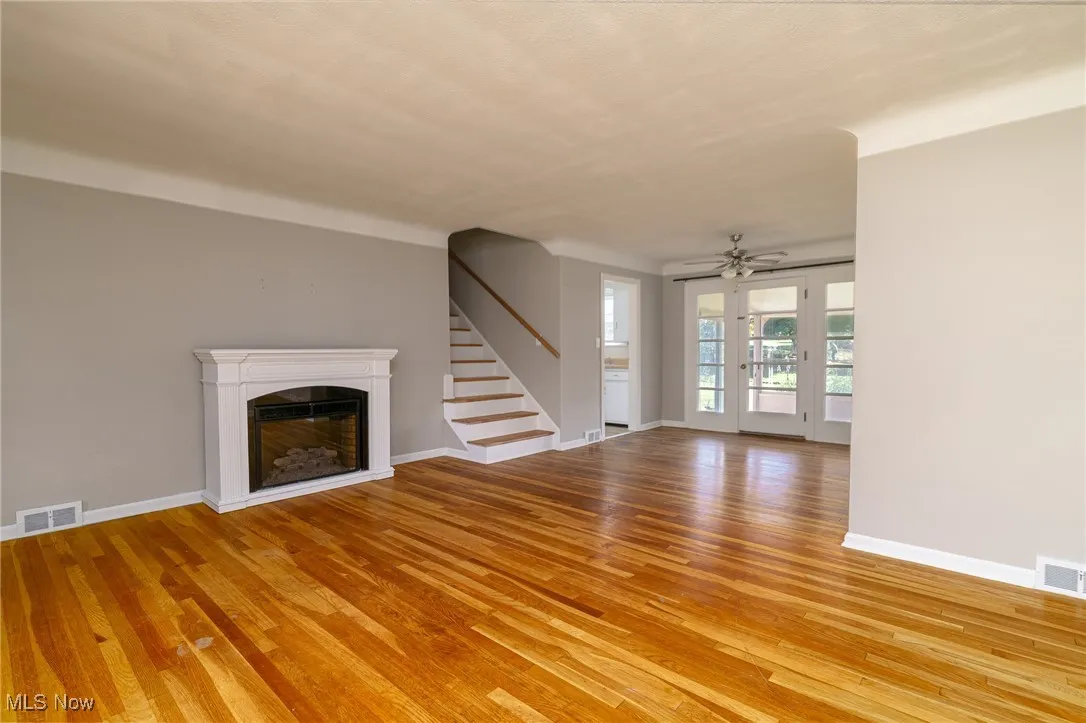 Unfurnished living room featuring a fireplace, light wood-type flooring, stairs, and ceiling fan
