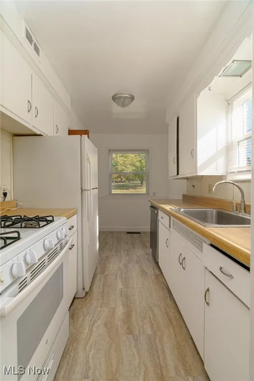 Kitchen with white cabinets, white appliances, light countertops, and light wood-style floors
