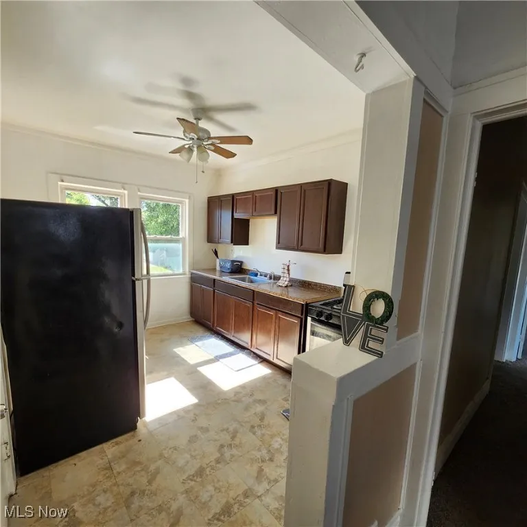 Kitchen with freestanding refrigerator, a ceiling fan, range with gas stovetop, and dark brown cabinetry
