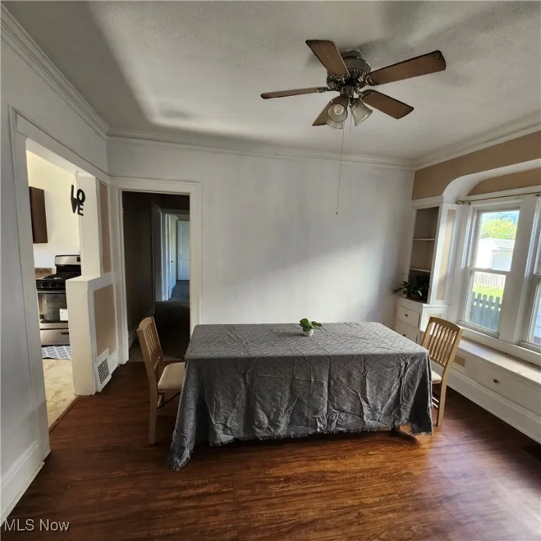Dining room featuring crown molding, dark wood-style floors, a textured ceiling, and a ceiling fan