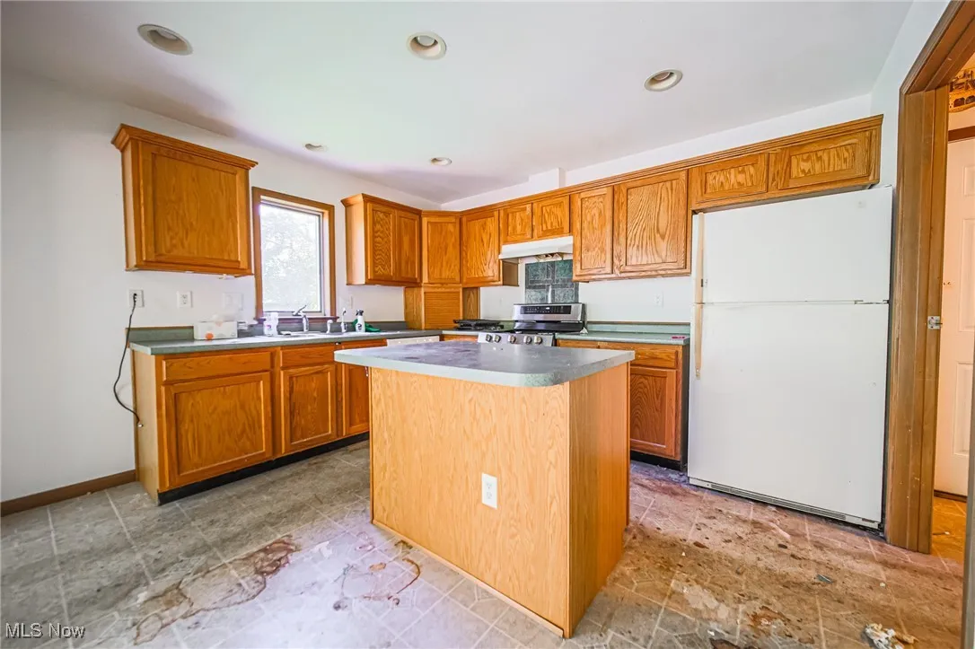 Kitchen featuring freestanding refrigerator, a center island, brown cabinetry, stainless steel stove, and recessed lighting