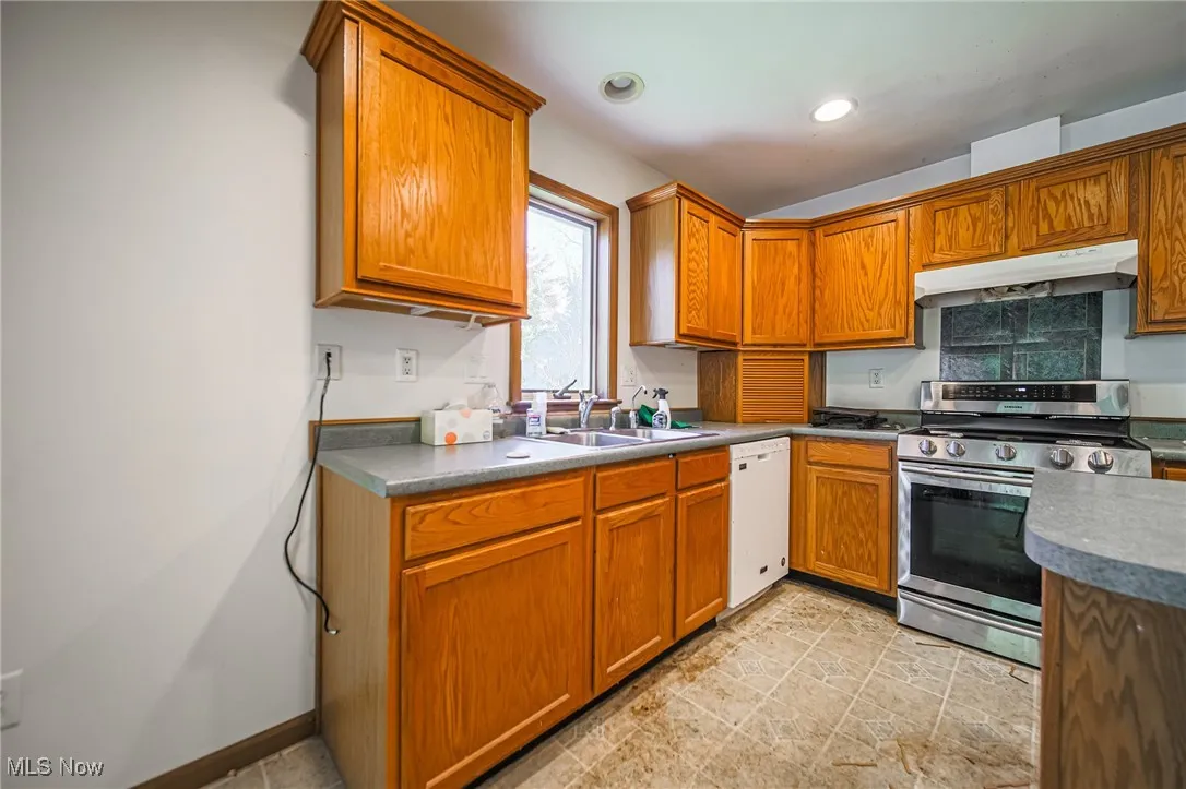 Kitchen featuring stainless steel gas range oven, brown cabinets, under cabinet range hood, white dishwasher, and recessed lighting