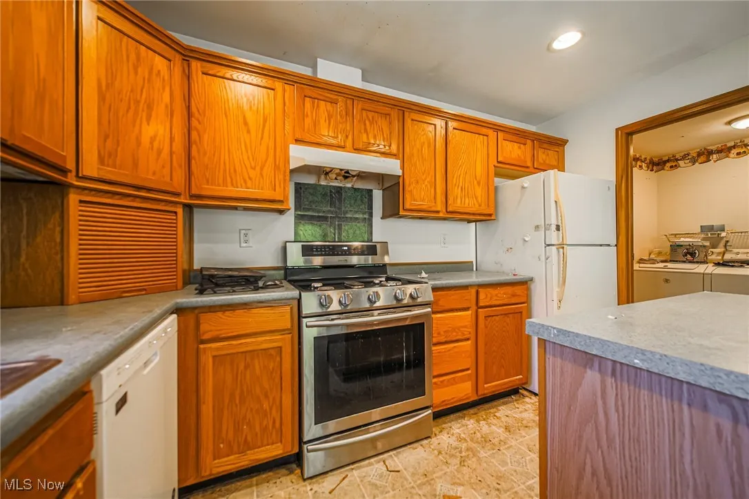 Kitchen with white appliances, under cabinet range hood, brown cabinets, recessed lighting, and washer / dryer