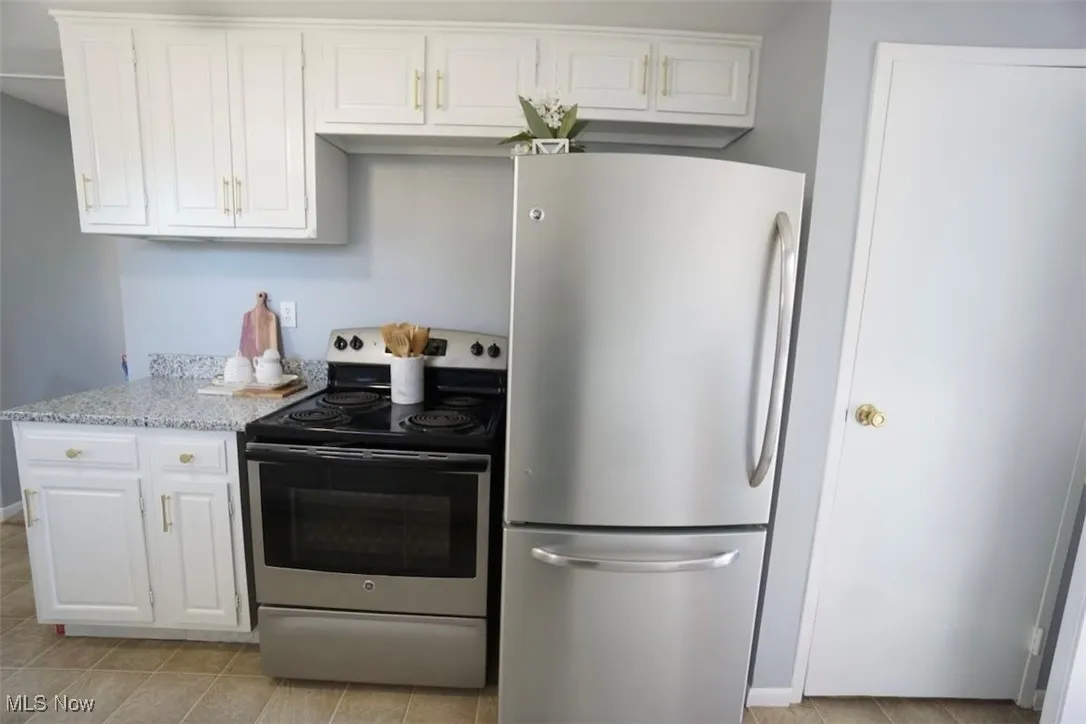 Kitchen with stainless steel appliances, white cabinetry, light tile patterned flooring, and light stone counters