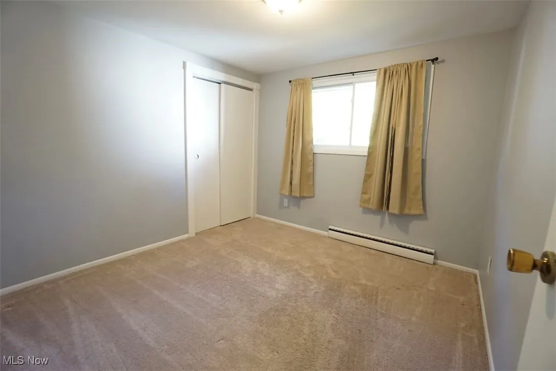 Unfurnished bedroom featuring carpet, a baseboard radiator, and a closet