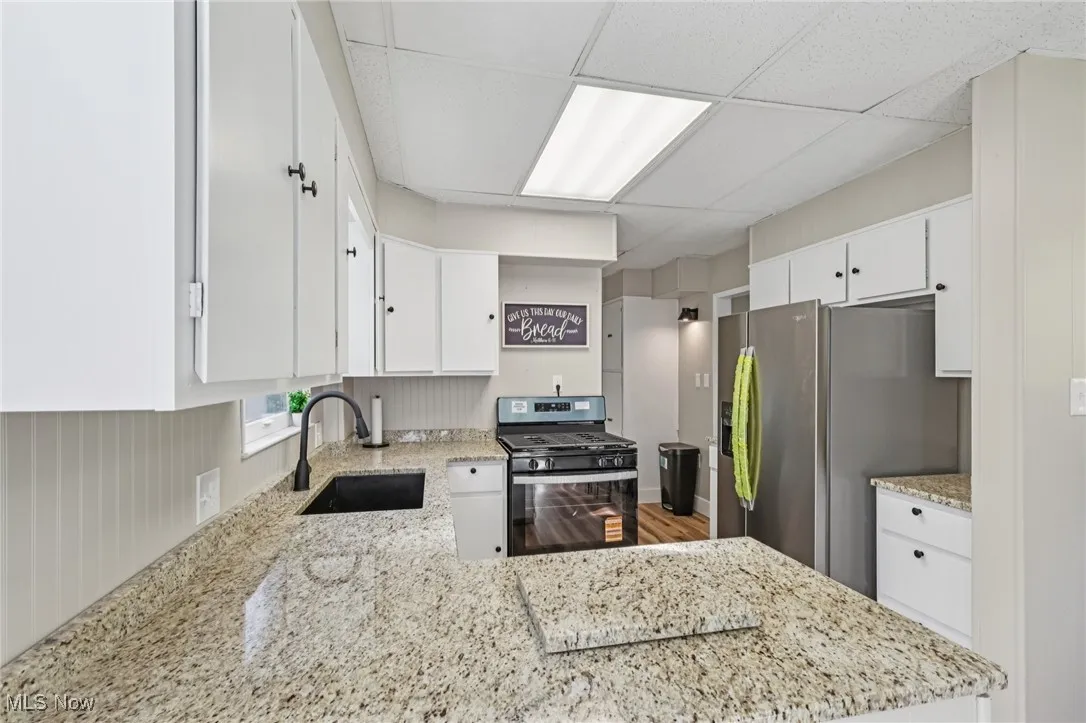 Kitchen featuring a paneled ceiling, appliances with stainless steel finishes, white cabinets, light stone countertops, and a peninsula
