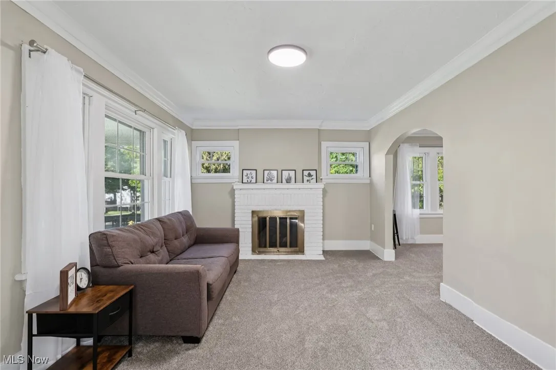 Living area with a brick fireplace, crown molding, carpet floors, and arched walkways