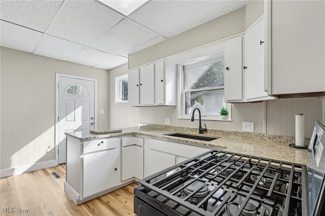 Kitchen with a peninsula, white cabinets, black range with gas cooktop, light wood-style flooring, and wood walls