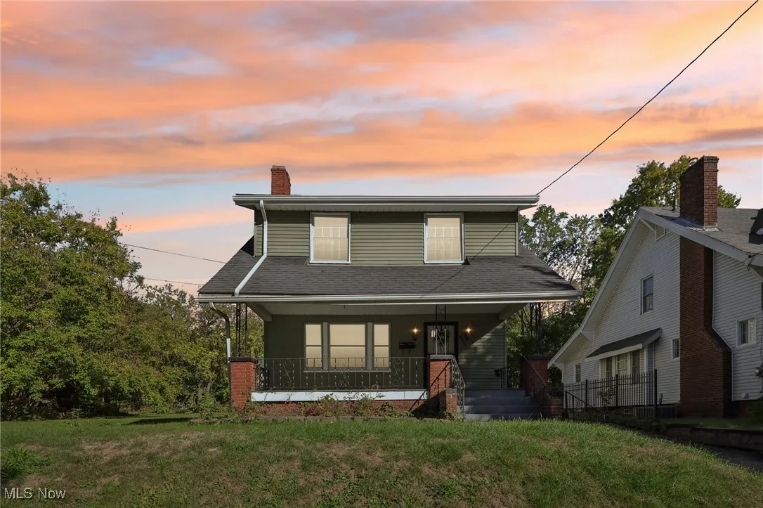 View of front of home with covered porch, a front yard, roof with shingles, and a chimney