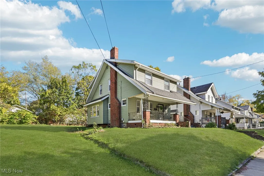 View of front of home featuring covered porch, a front yard, and a chimney