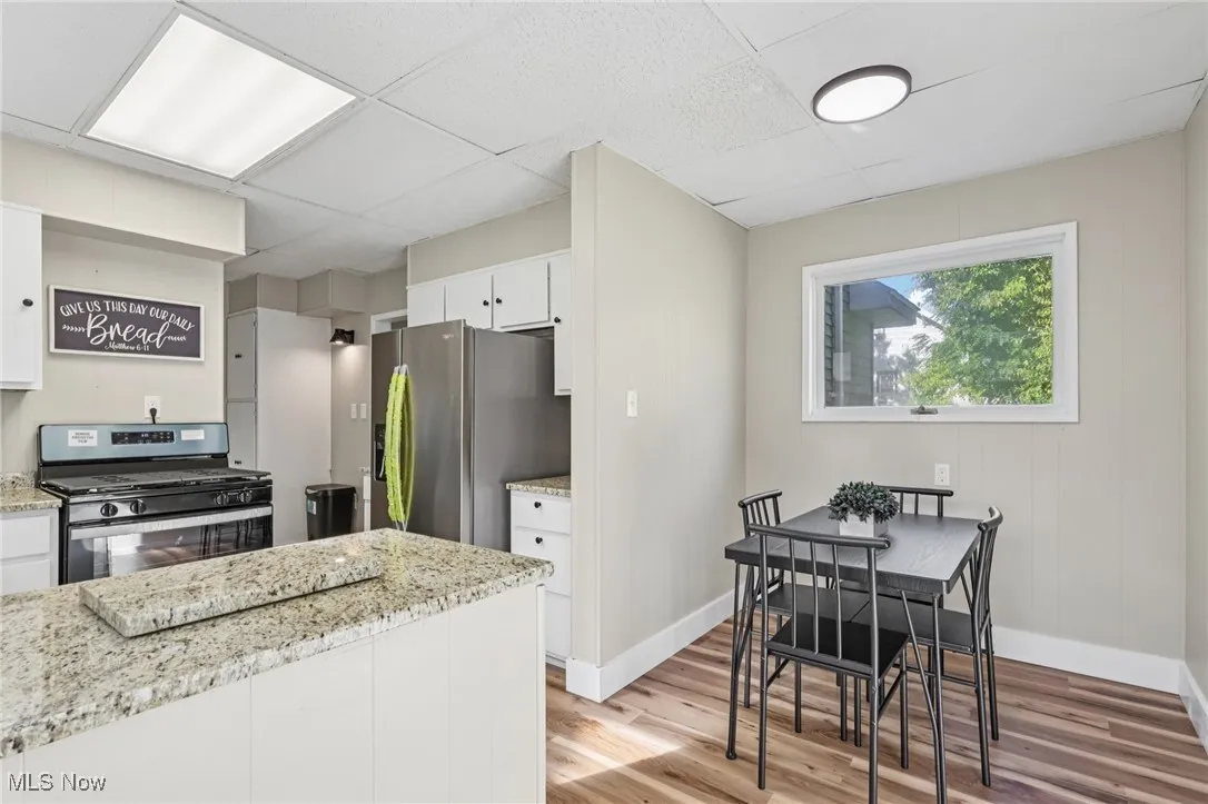 Kitchen with appliances with stainless steel finishes, light stone counters, white cabinets, light wood-style floors, and a paneled ceiling
