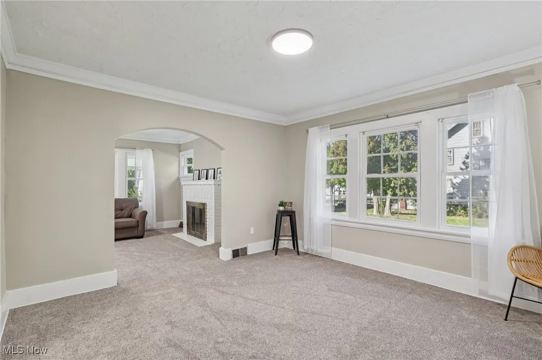 Unfurnished living room featuring light carpet, crown molding, a brick fireplace, and arched walkways