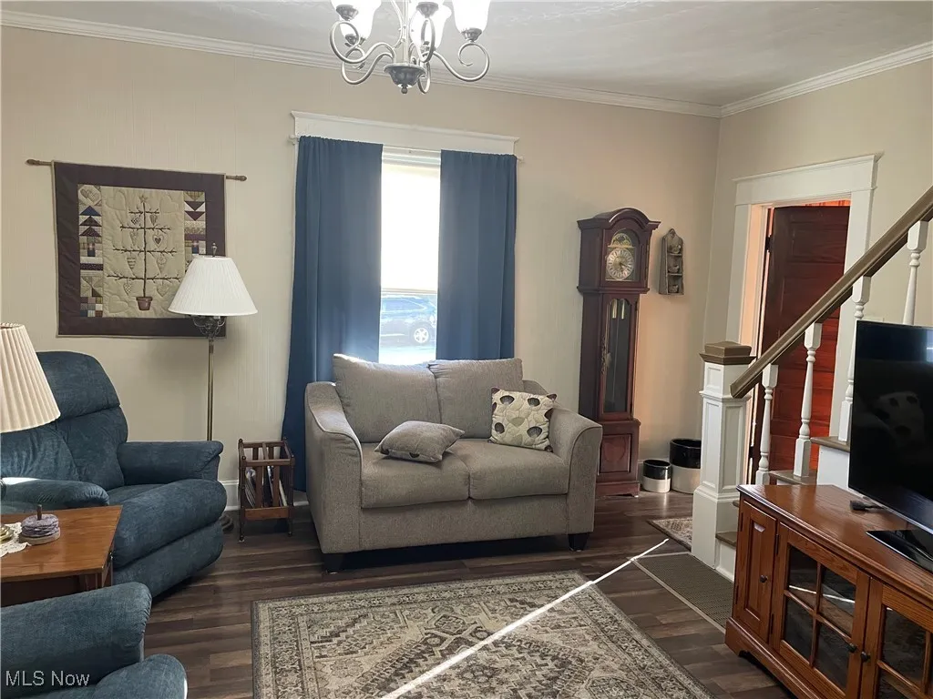Living area with stairway, ornamental molding, dark wood-type flooring, and a chandelier