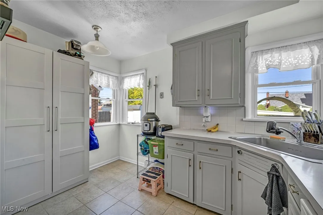 Kitchen featuring light countertops, healthy amount of natural light, light tile patterned floors, tasteful backsplash, and a textured ceiling