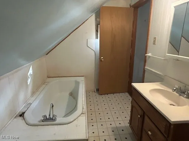 Full bathroom featuring a tub, vanity, light flooring, and lofted ceiling