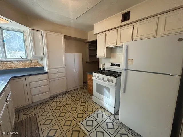 Kitchen with white appliances, dark countertops, and white cabinetry