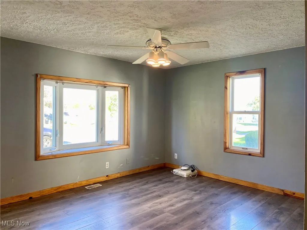 Empty room with a textured ceiling, hardwood / wood-style flooring, and a ceiling fan